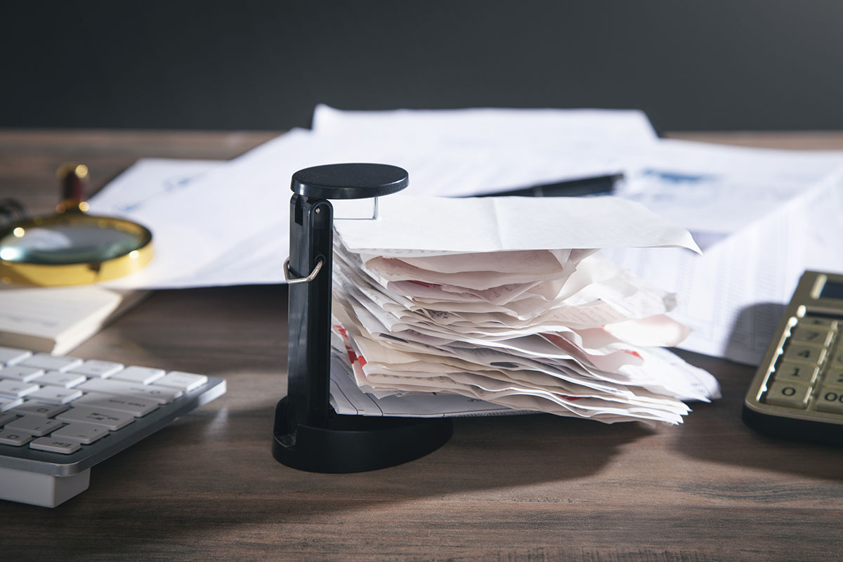 A stack of bills and receipts on a desk spike beside a calculator and keyboard